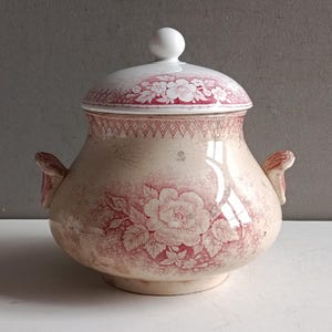 May include: A vintage ceramic lidded serving dish with a floral design in red and white. The dish has two handles and a round knob on the lid. The floral pattern includes roses and other flowers.