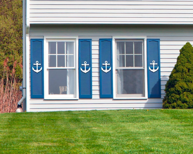 May include: A white house with three windows with blue shutters and white anchor accents. The windows are on the front of the house and have white trim. The house is surrounded by green grass.