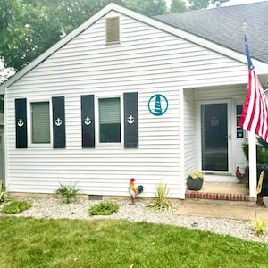 May include: A white house with black shutters and a blue lighthouse sign. The house has a front door with a glass panel and a small porch. There is a red rooster statue in the front yard.