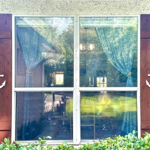 May include: A window with brown wooden shutters and white anchors on each side. The window has a white frame and is divided into four panes. The window is covered with a blue curtain.