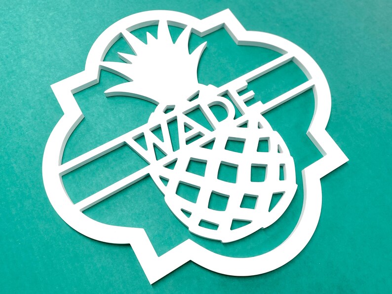 Może przedstawiać: Biały drewniany znak w kształcie ananasa z wyciętym w środku imieniem "Wade". Znak ma ozdobną, falistą ramkę.