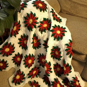 May include: A white crocheted throw blanket with red, green, and yellow poinsettia flower designs.
