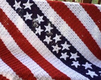 May include: A crocheted blanket in the colors of the American flag. The blanket is made with red, white, and blue yarn and features a diagonal pattern of stars.