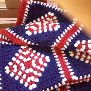 Pu&ograve; includere: Una coperta all'uncinetto con un motivo a quadrati della nonna rosso, bianco e blu.