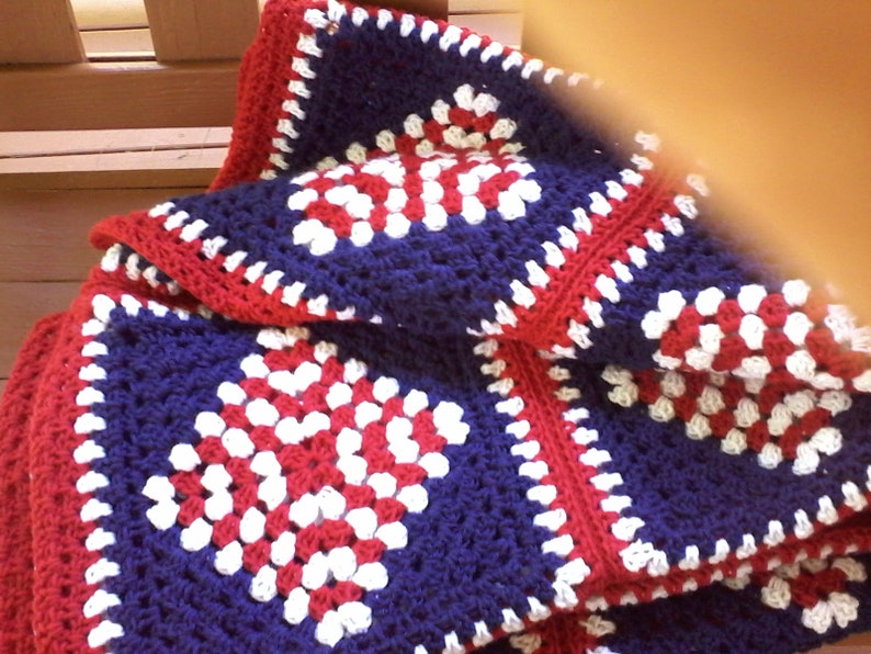Pu&ograve; includere: Una coperta all'uncinetto con un motivo a quadrati della nonna rosso, bianco e blu.