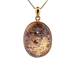 May include: A gold-colored necklace with an oval pendant. The pendant features a clear, oval-shaped stone with a mix of brown, purple, and gold inclusions. The chain is a delicate, gold-colored link chain.