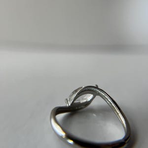 May include: A silver ring with a marquise-cut clear gemstone. The band curves gracefully, and the gemstone is set in a prong setting. The ring is shown against a white background.