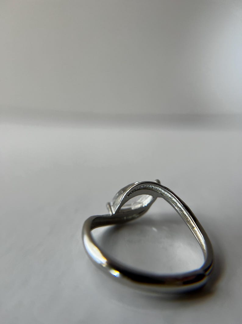 May include: A silver ring with a marquise-cut clear gemstone. The band curves gracefully, and the gemstone is set in a prong setting. The ring is shown against a white background.