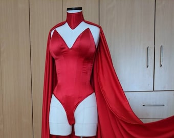 May include: A red satin bodysuit with a high collar and a matching cape. The bodysuit has a sweetheart neckline and a fitted silhouette. The cape is long and flowing.