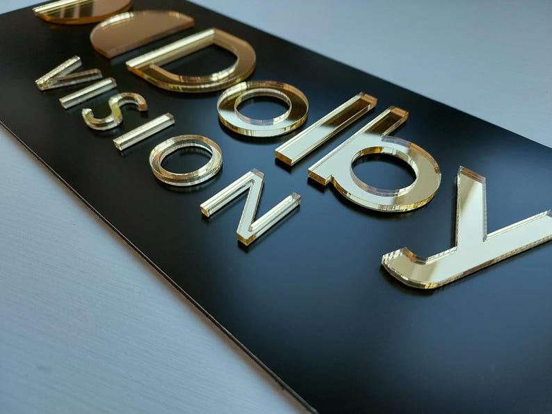 Peut inclure: Un panneau rectangulaire noir avec l'inscription "VISION BOARD" en lettres dor&eacute;es miroir. Les lettres sont en relief et refl&egrave;tent la lumi&egrave;re, cr&eacute;ant un effet brillant. Le panneau est probablement destin&eacute; &agrave; la d&eacute;coration de la maison ou du bureau.