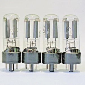 May include: Four vintage vacuum tubes with clear glass bulbs and black bases. Each tube has internal components visible, including vertical metal plates and a wire mesh. The tubes are labeled with numbers and letters, likely model designations.