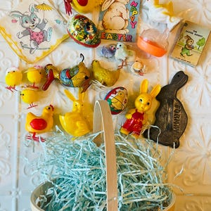 May include: An assortment of Easter-themed decorations, including a basket filled with blue paper, vintage toys, and a handkerchief with a bunny illustration. The toys include chicks, ducks, and bunnies in various colors.
