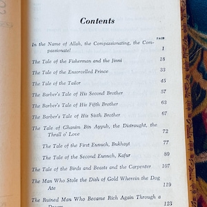 May include: Open book displaying a table of contents titled "Contents". The page is aged with a gold border and lists chapter titles such as "The Tale of the Fisherman and the Jinni" and "The Tale of the Ensorcelled Prince".