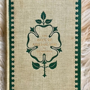 May include: The cover of a vintage book titled "The Days of Auld Lang Syne" by Ian Maclaren. The cover features a green clover design with a gold border.