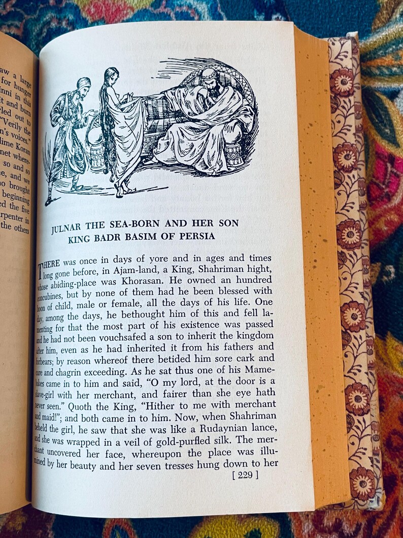 May include: Open book page with an illustration of three figures in a Middle Eastern setting. The text reads "JULNAR THE SEA-BORN AND HER SON KING BADR BASIM OF PERSIA" with additional text below. The book's edge has a floral pattern.