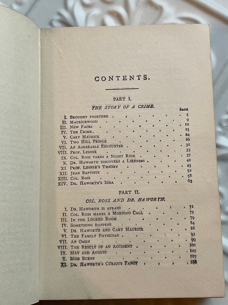 May include: A black and white book with the title "CONTENTS" printed on the cover. The book is open to a page with a list of chapter titles and page numbers. The chapters are divided into two parts: "The Story of a Crime" and "Col. Ross and Dr. Haworth".