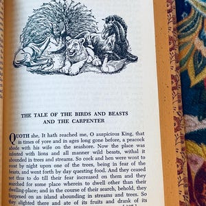 May include: Open book with a black and white illustration of a peacock, lion, horse, and other animals. The text "THE TALE OF THE BIRDS AND BEASTS AND THE CARPENTER" is above the illustration. The page is yellowed.