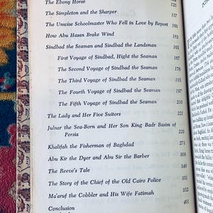 May include: Open book with a contents page featuring a list of stories, including "Sindbad the Seaman" and "The Ebony Horse." The page numbers are listed on the right side. The book's edges are aged with a decorative border.