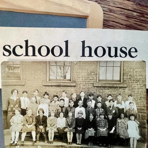 May include: A vintage black and white photograph of a 4th grade class at Prospect St School in Ashtabula, Ohio. The image shows a group of children and an adult posed in front of a brick building with windows, with the text school house above.