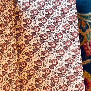 May include: Open book with a floral pattern. The pages display a repeating design of reddish-brown flowers and leaves on a cream background. The book's binding is visible on the left side. The overall aesthetic is vintage.