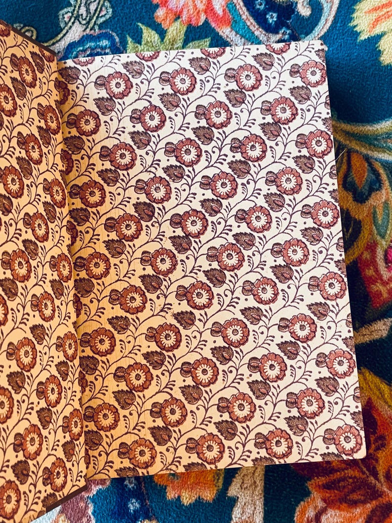 May include: Open book with a floral pattern. The pages display a repeating design of reddish-brown flowers and leaves on a cream background. The book's binding is visible on the left side. The overall aesthetic is vintage.