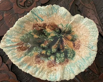 May include: A ceramic dish shaped like a large leaf with a textured surface. The glaze features a blend of light blue, tan, and dark green colors, with a prominent crack running across the right side of the leaf-shaped ceramic piece.