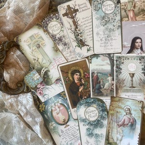 May include: A collection of vintage religious cards with floral and cross motifs. The cards feature illustrations of Jesus, Mary, and other religious figures. Some cards have the text "Happy Feast" and other religious text.