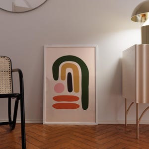 May include: A framed abstract art print with a white border. The artwork features a design of colorful shapes, including a green arch, a yellow arch, a black vertical rectangle, a pink circle, and two orange horizontal lines, set against a light pink background.