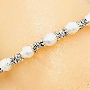 May include: A white pearl bracelet with silver accents. The bracelet is made of small, round pearls and silver beads.