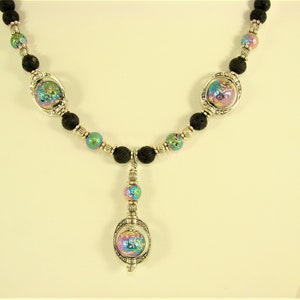 May include: A silver necklace with three iridescent glass orbs and black lava rock beads. The necklace has a pendant with a larger iridescent glass orb.