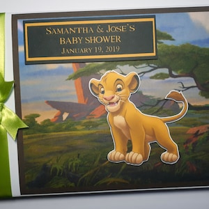 Könnte beinhalten: Gästebuch für eine Babyparty mit einem Simba-Ausschnitt aus Der König der Löwen. Das Cover hat eine Landschaftsszene und ein grünes Band und eine Schleife. Der Text lautet "SAMANTHA & JOSE'S BABY SHOWER JANUARY 19, 2019."