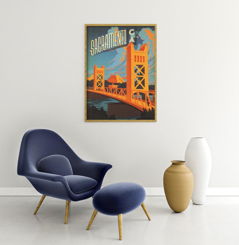 May include: A vintage travel poster featuring a stylised illustration of the Tower Bridge in Sacramento, California. The poster is in a wooden frame and has a blue, orange and yellow colour scheme. The text "Sacramento CA" is printed in a bold, stylised font at the top of the poster.