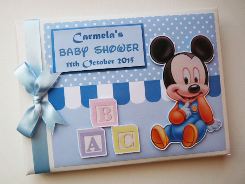 May include: A baby shower invitation with a blue and white polka dot and striped design. The invitation features a Mickey Mouse graphic and the text "Carmela's BABY SHOWER 11th October 2015". A light blue ribbon and bow are tied on the left side.