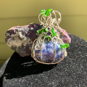 May include: A silver wire wrapped pendant featuring a blue and white sodalite stone with green glass accents.