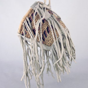 May include: A small, woven basket with a fringe of white leather. The basket is hanging from a white cord.