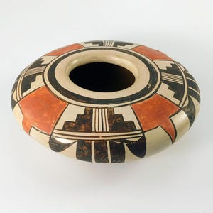 May include: A hand-painted, oval-shaped pottery vessel with a wide opening. The design features geometric patterns in black, orange, and cream colors. The vessel is likely used for decorative purposes.