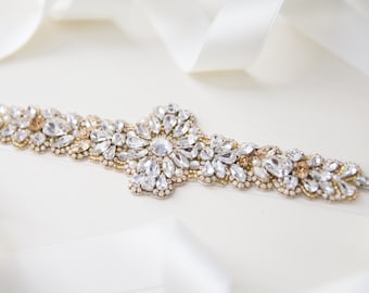 May include: A delicate bridal belt with a floral design featuring clear and gold-toned rhinestones and pearls.