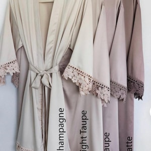 May include: Four satin robes in different shades of beige, from lightest to darkest: Champagne, Light Taupe, Taupe, and Latte. Each robe has delicate lace trim around the sleeves and hem.