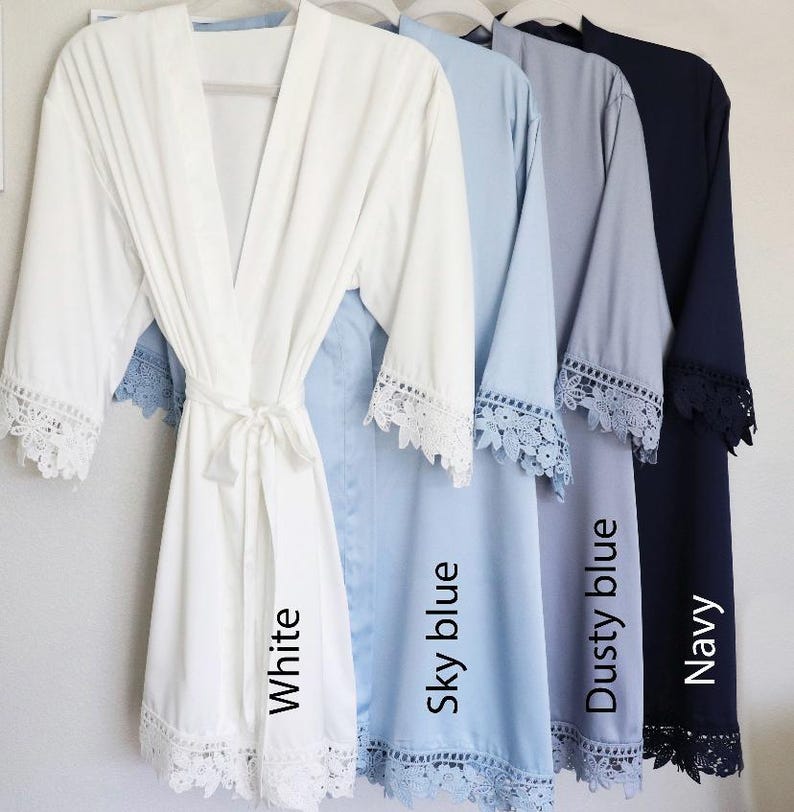 May include: Five satin robes with lace trim in white, sky blue, dusty blue, and navy. The robes are arranged from left to right with the colours listed. The robes have a tie at the waist and are labelled with the colour name.