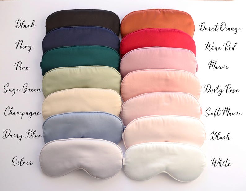 May include: A collection of sleep masks in various colors, including black, navy, and burnt orange. The image displays the masks in a neat arrangement, with each mask showcasing a different shade. Text labels identify each color, such as "Wine Red" and "Dusty Rose."