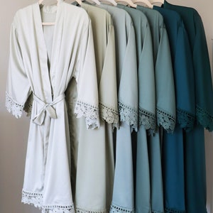 May include: A set of eight satin robes with lace trim in shades of green and blue. The robes are arranged in a gradient from light green to dark blue.