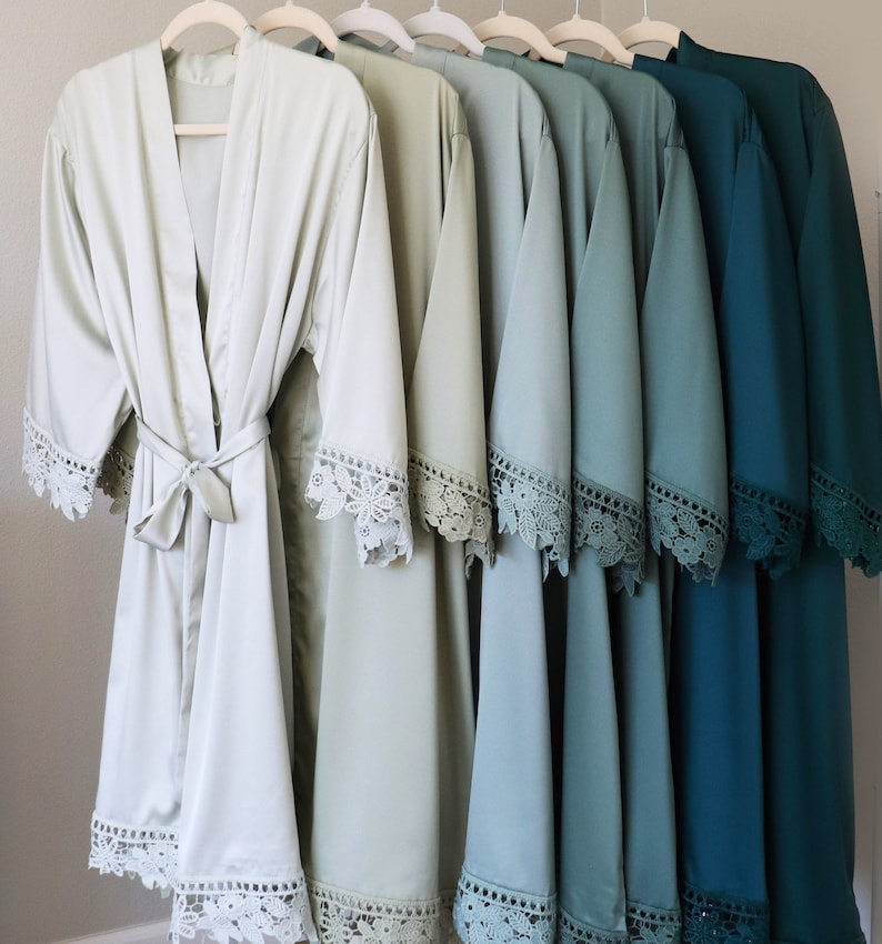 May include: A set of eight satin robes with lace trim in shades of green and blue. The robes are arranged in a gradient from light green to dark blue.