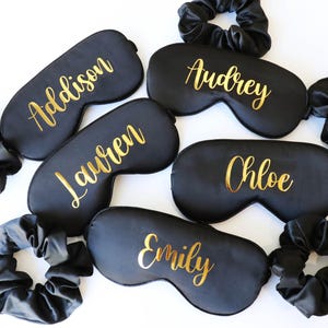 May include: Black sleep masks with gold lettering, each bearing a different name: Addison, Audrey, Lauren, Chloe, and Emily. Matching black scrunchies are also included. These items are likely for a bridal party or a group gift.
