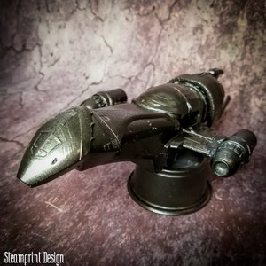 May include: A black and silver model of a spaceship with a detailed design. The spaceship is on a black stand.