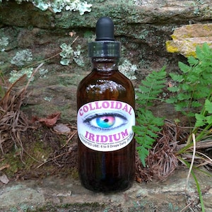 May include: A brown glass bottle with a dropper top and a white label that says "Colloidal Iridium". The label has a colorful eye graphic. The bottle is sitting on a rock with green plants around it.