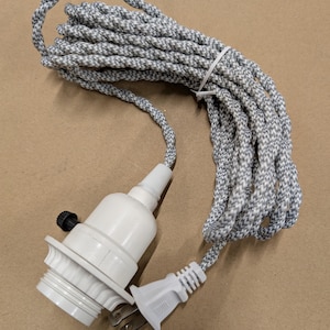 May include: A white light bulb socket with a black rotary switch attached to a long, coiled electrical cord featuring a grey and white chevron-patterned fabric covering and a standard two-prong white electrical plug at the end of the cord.