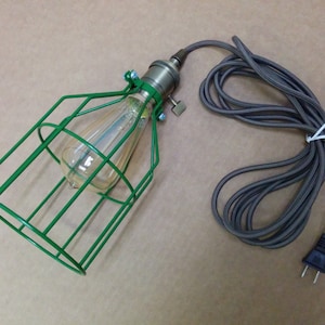 May include: A green metal cage light fixture with a clear light bulb and a gray cord with a plug.