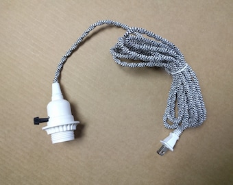 May include: A white electrical cord with a black and white braided fabric covering. The cord has a standard plug on one end and a white ceramic light socket on the other end.