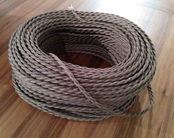 May include: A coil of gray twisted electrical wire. The wire is tightly wound, creating a circular shape. The texture of the wire is visible, with the individual strands of the twist clearly defined. The wire is a neutral color, suitable for various applications.