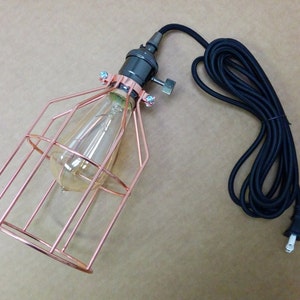 May include: A copper wire cage pendant light with a black cord and plug. The light has a clear glass bulb inside.